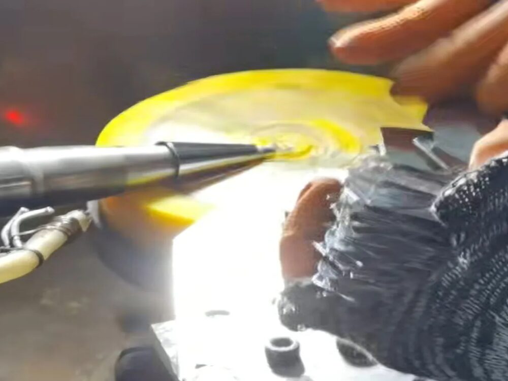 Worker buffing metal parts by hand against a rotating polishing wheel