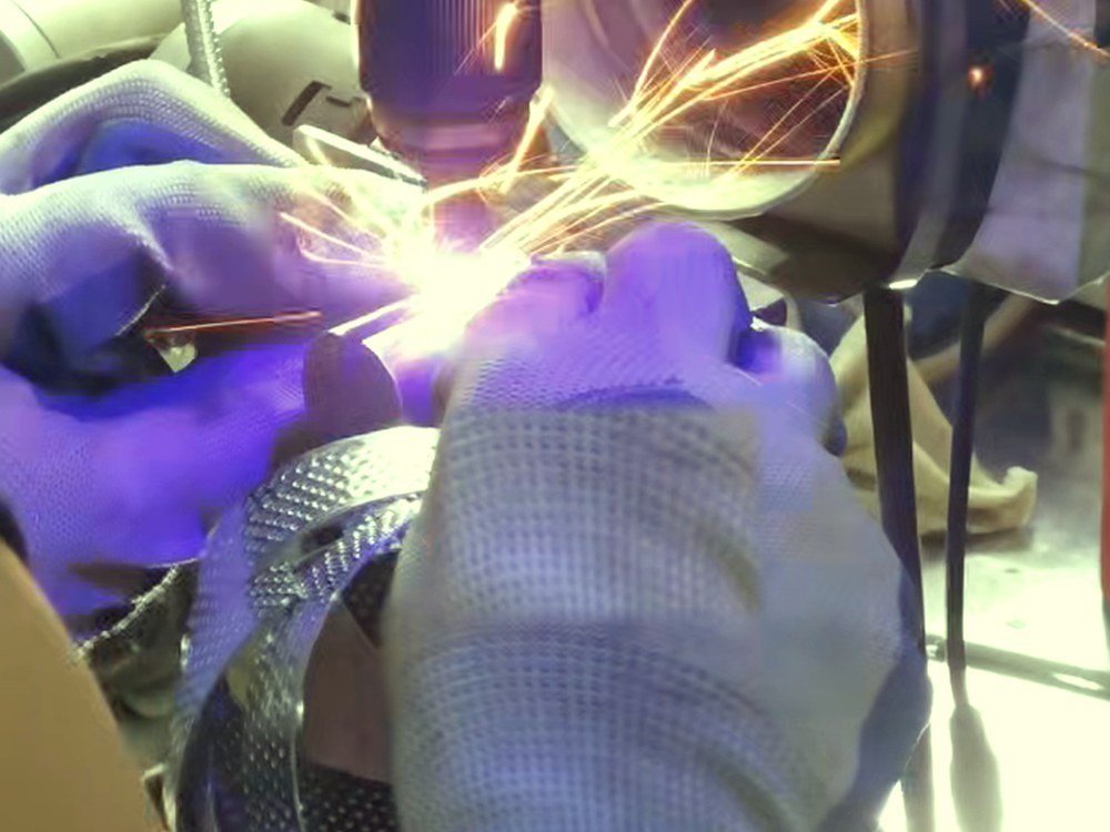 Worker dressing a nozzle joint by hand on a rotary tool, sparks flying